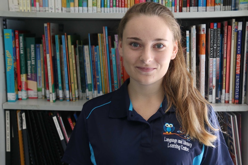 Jasmine Vikan smiles at the camera, wearing her school uniform, in the school library.