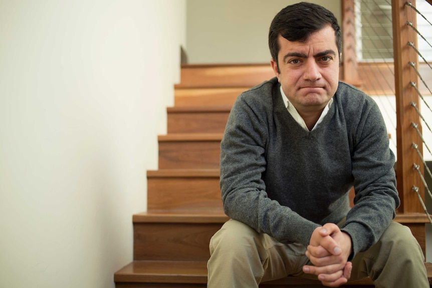 A man with a smirk on his face sits on a set of stairs