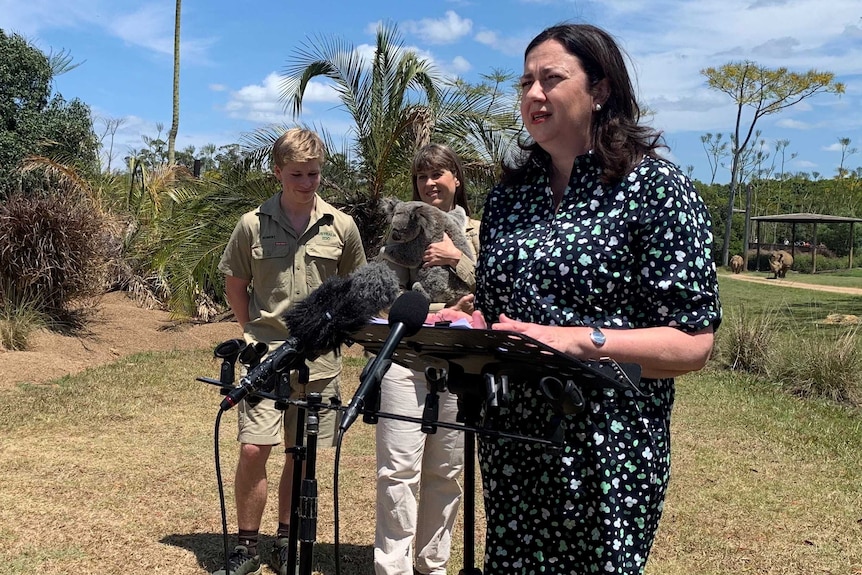 Robert and Terri Irwin (holding a koala) standing next to the Premier speaking at a lectern