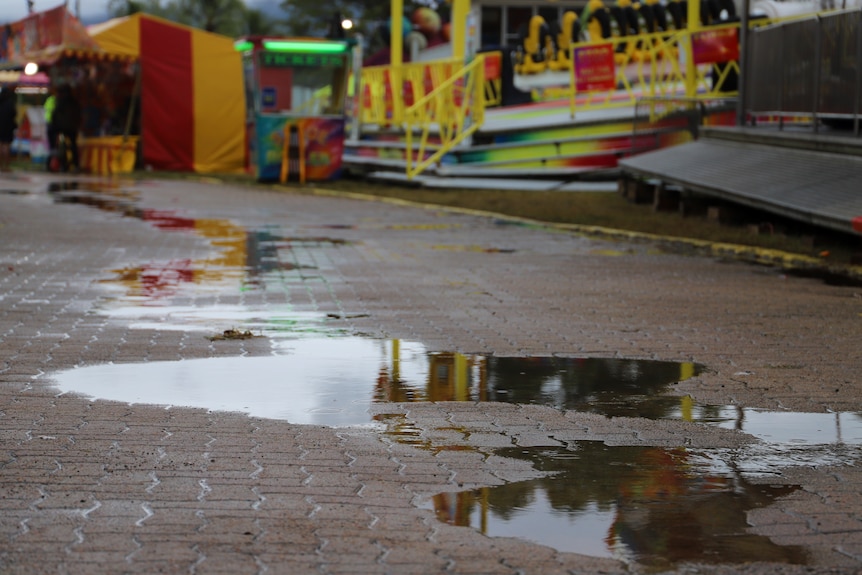 big puddles blanket pavement, colourful show equipment in the background. 