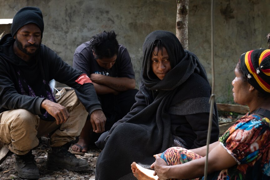 A women draped in black blankets sits surrounded by three others