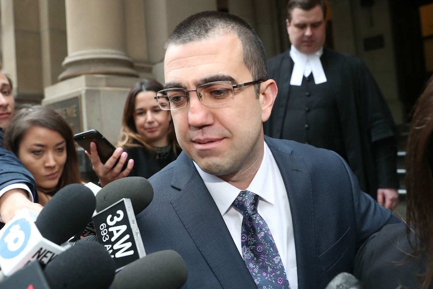 Faruk Orman, wearing glasses and a suit, walks out of court as he is filmed and photographed by media.