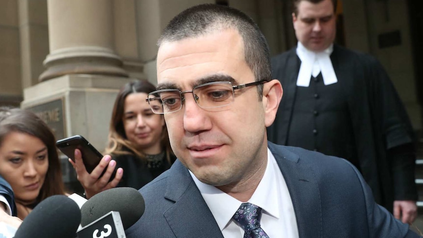 Faruk Orman, wearing glasses and a suit, walks out of court as he is filmed and photographed by media.