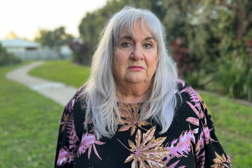 A woman wearing a floral top stands outside.