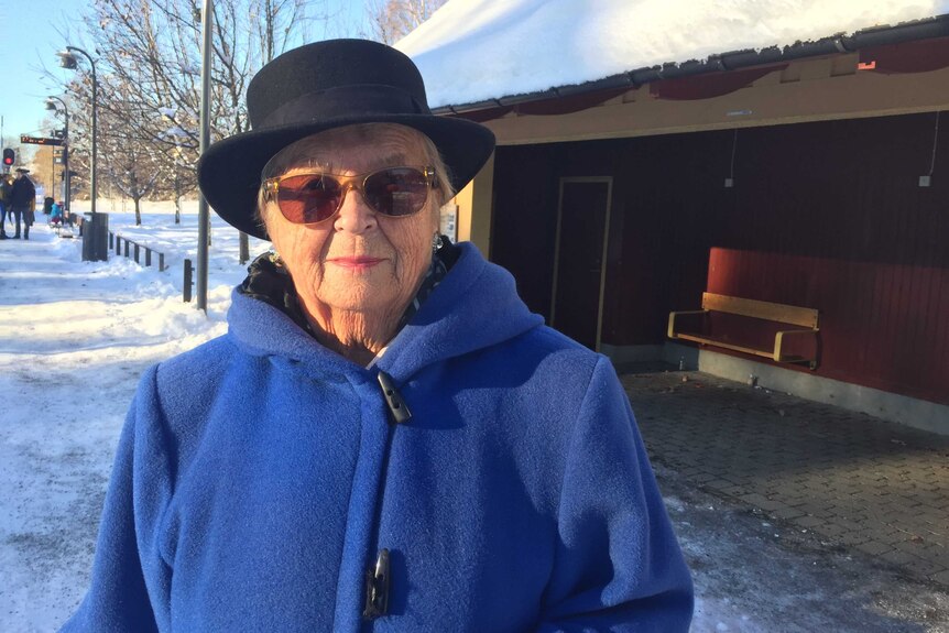 Johan's mother Gunilla stands on a snow-covered street wearing a blue coat and a black hat.