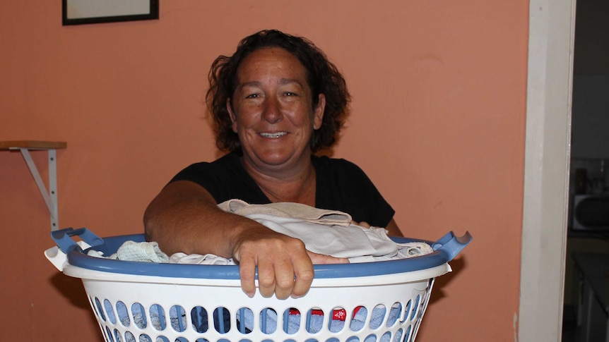 A smiling woman holds a washing basket.