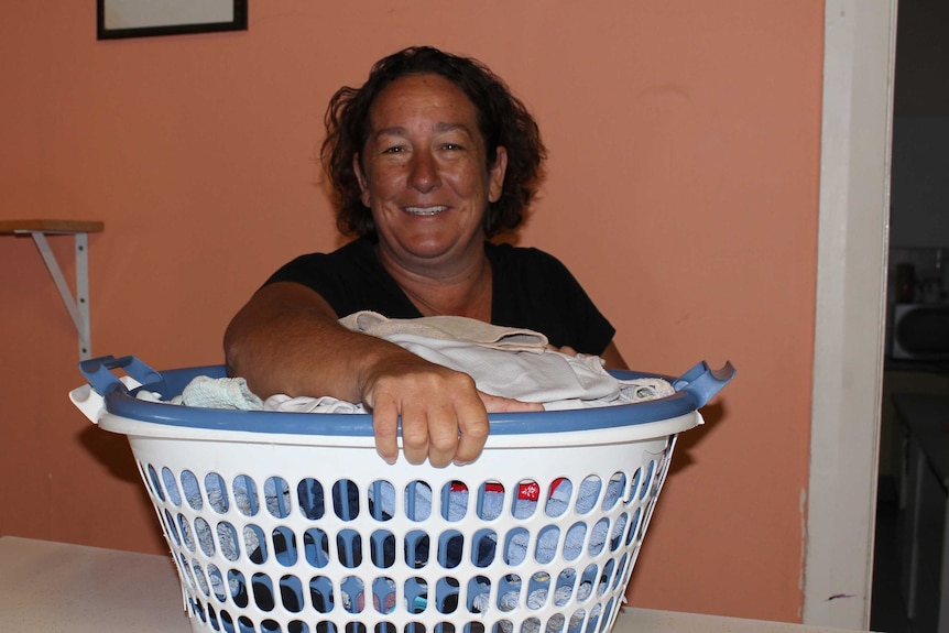 A smiling woman holds a washing basket.