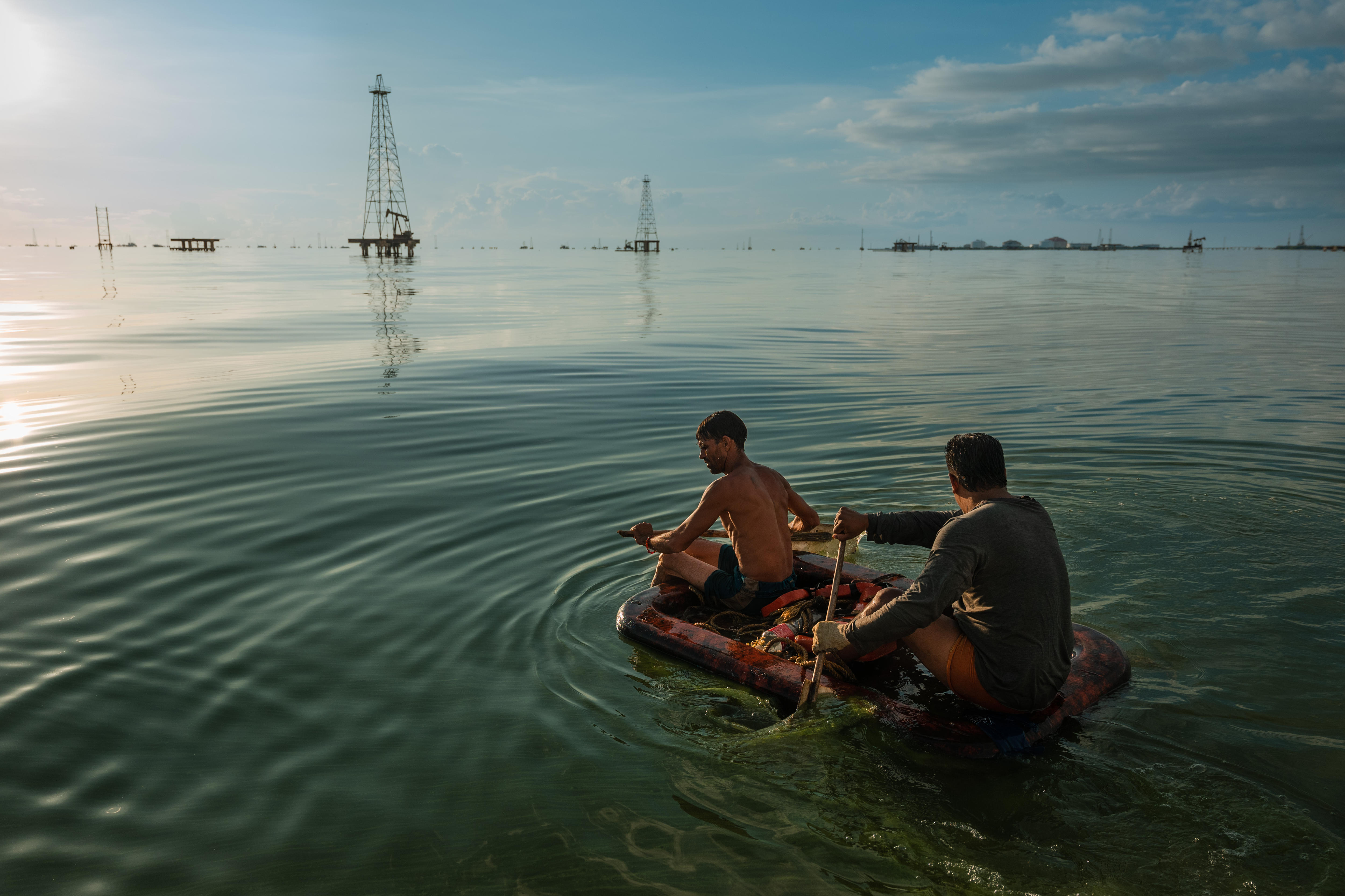 Two fishermen paddle through the green waters of Lake Maracaibo