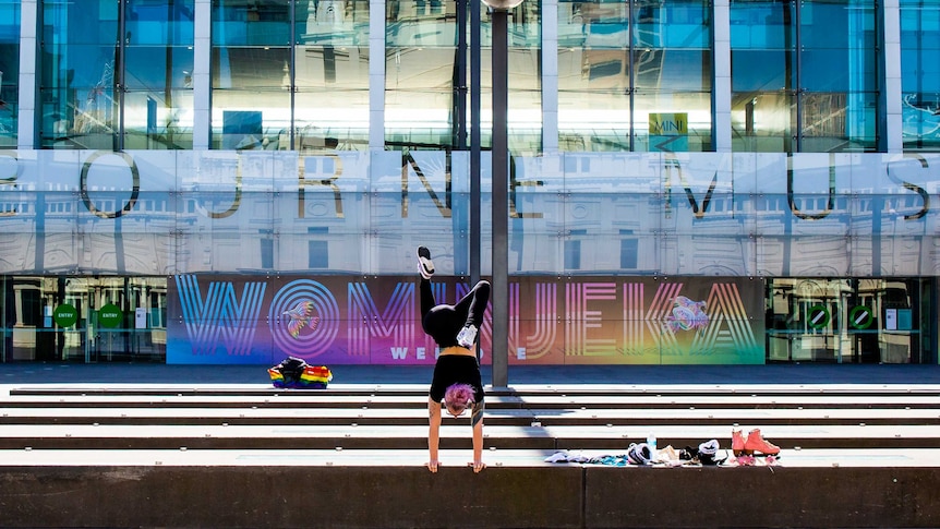 A woman does a handstand in front of the Melbourne Museum.