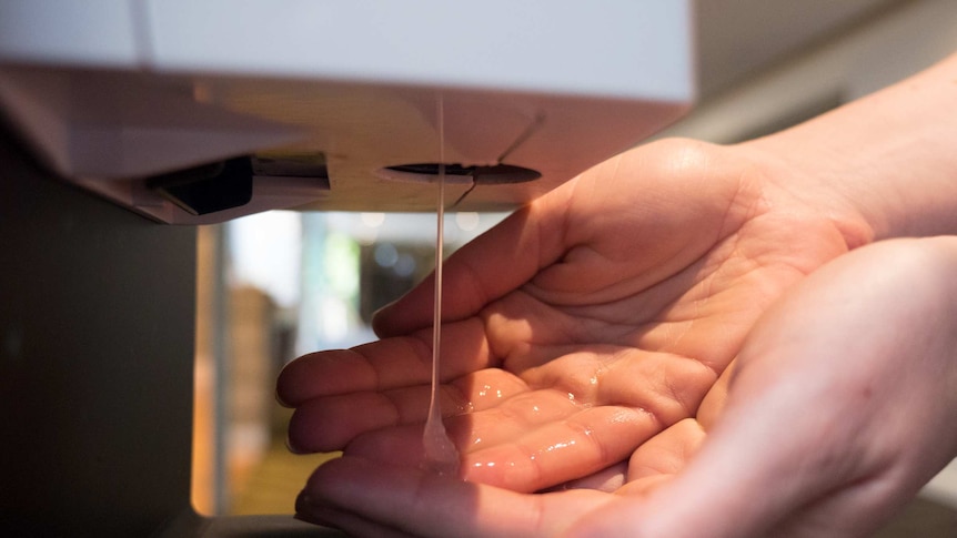 A person has antiseptic gel from a hand sanitiser unit dropped on their hands.