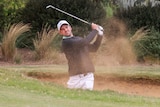 A golfer standing in a bunker looks down the fairway as he completes a shot from the sand in a practice round.