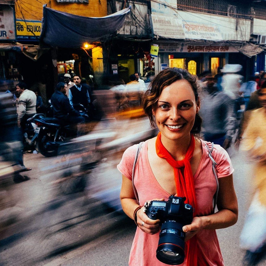 Photojournalist Jane Cowan holding camera on a street in India with a blurred background.