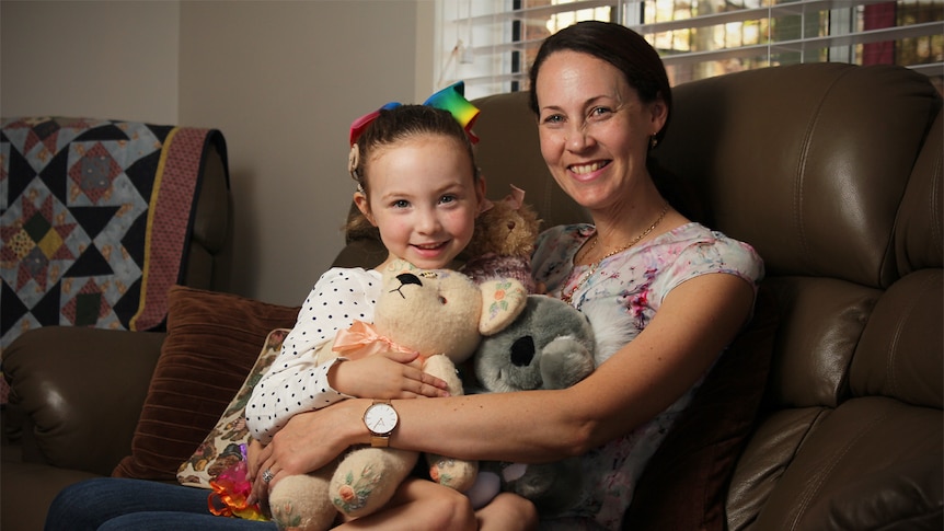 Hayley Ryan sits on her mother Melissa's lap with her teddy bears on the family couch.