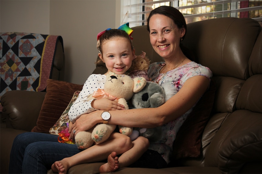 Hayley Ryan sits on her mother Melissa's lap with her teddy bears on the family couch.