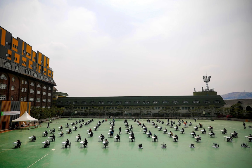 A photo of people sitting at desks in the open-air courtyard between two buildings