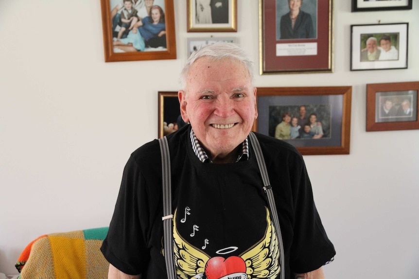 Frank Roberts, 91, is photographed in his loungeroom wearing his choir uniform - a black t-shirt with a heart logo.