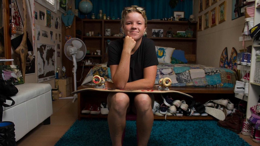 Image of Poppy sitting on her bed with a skateboard on her lap.
