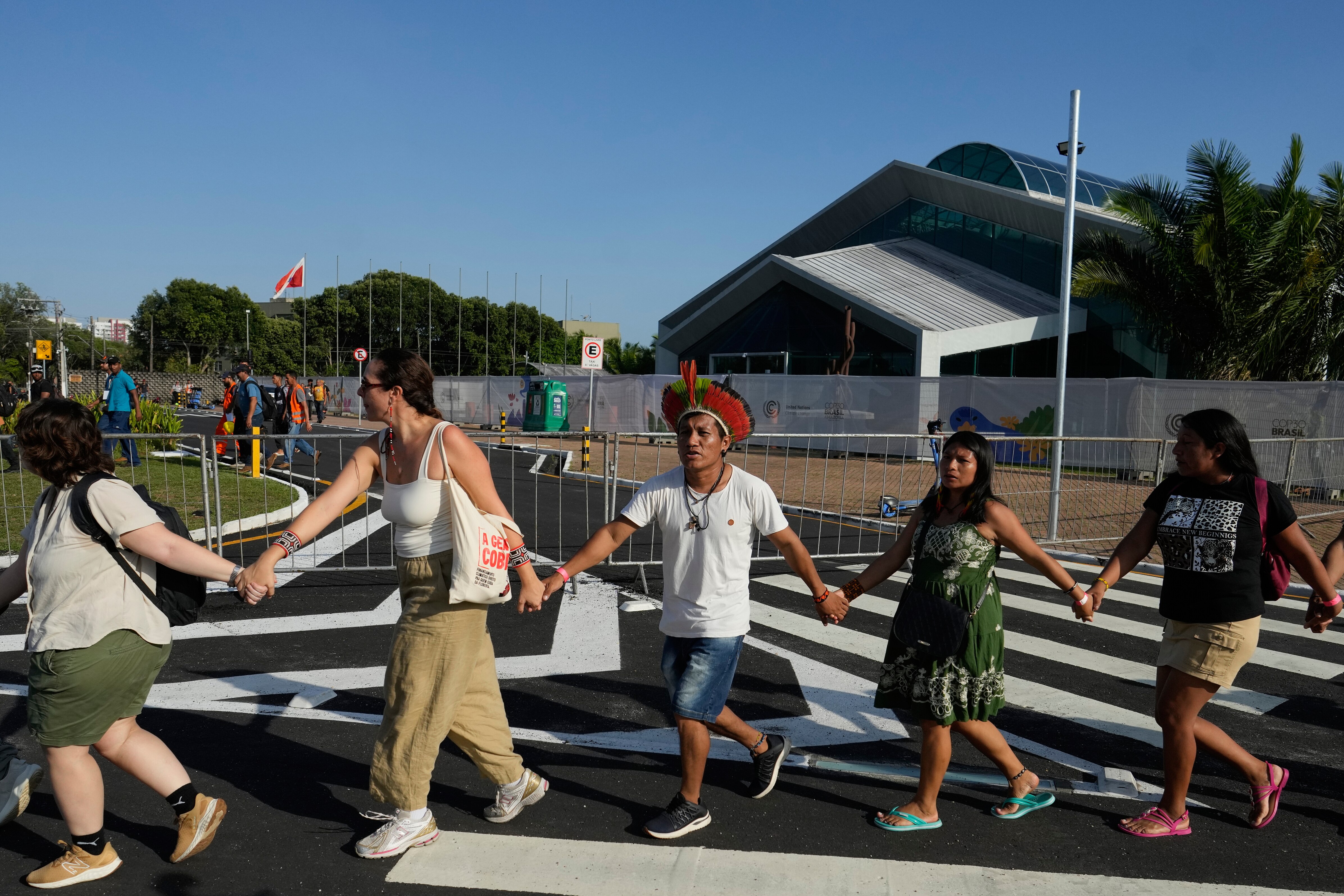 A group of people holding hands walking across a road in front of barricades.