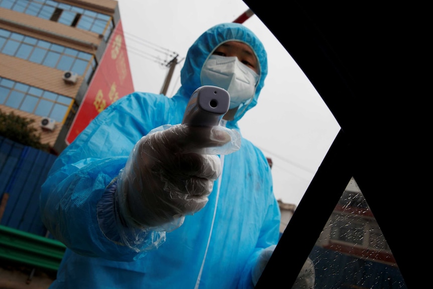 A medical worker holds a thermometer to check a passenger's temperature at a checkpoint