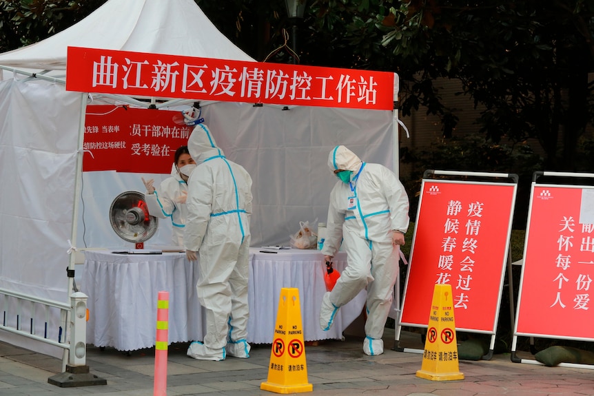 Government workers in protective clothing gather at a work station for pandemic control outside a residential block.