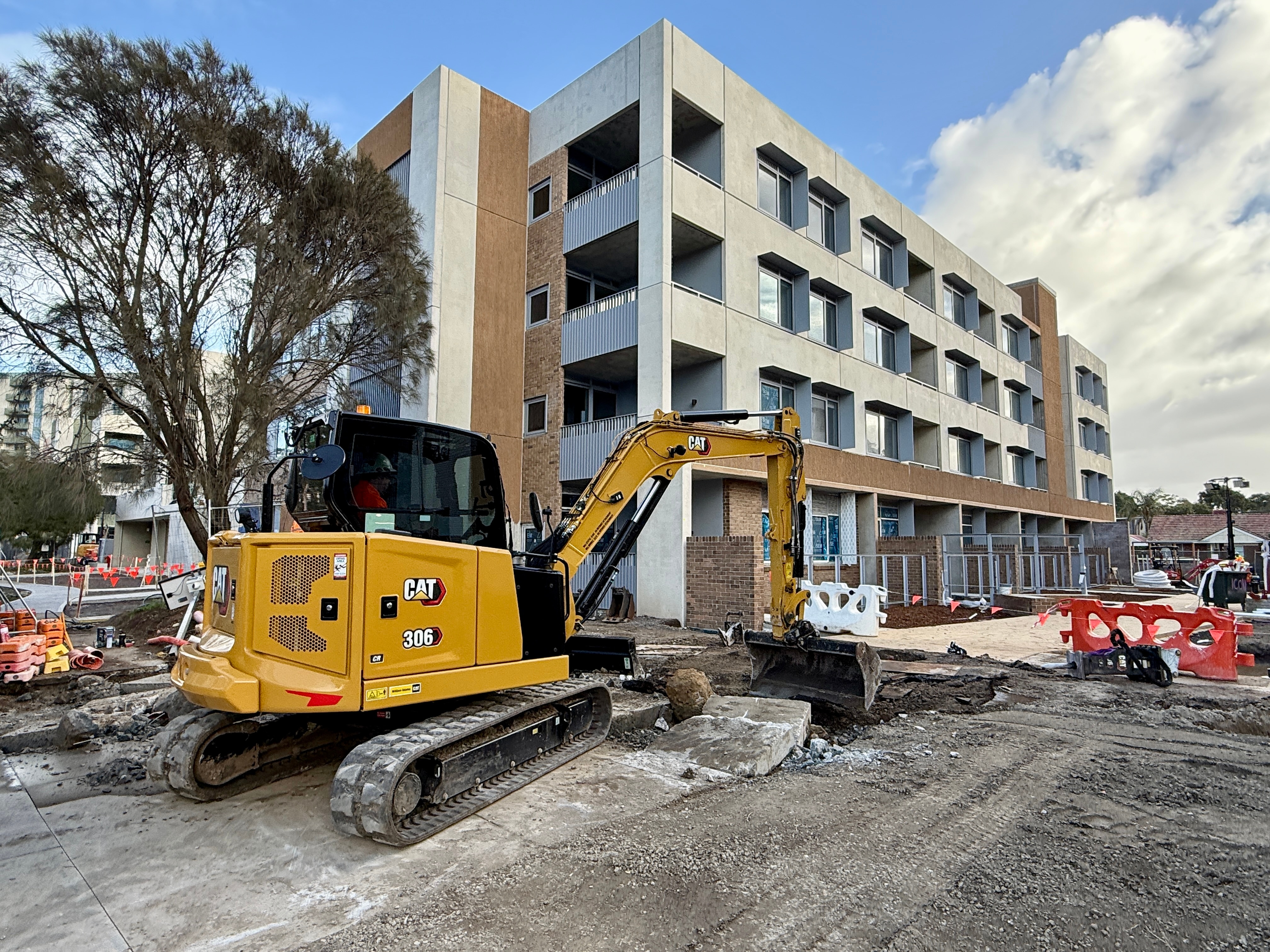 A bulldozer sits on broken ground next to tower block apartment