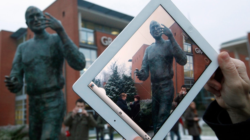 A man takes photos of a statue of the late Apple co-founder, Steve Jobs, with his iPad.