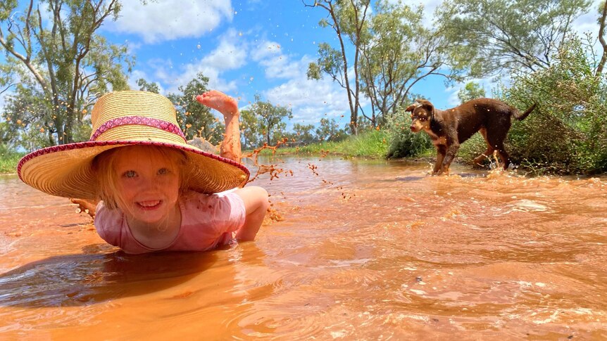 Lucy Sharplin and dog Buddy playing in puddles of orange at Toompine, south of Quilpie