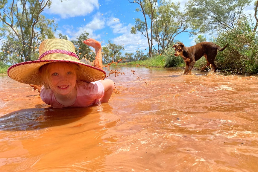 Lucy Sharplin and dog Buddy playing in puddles of orange at Toompine, south of Quilpie