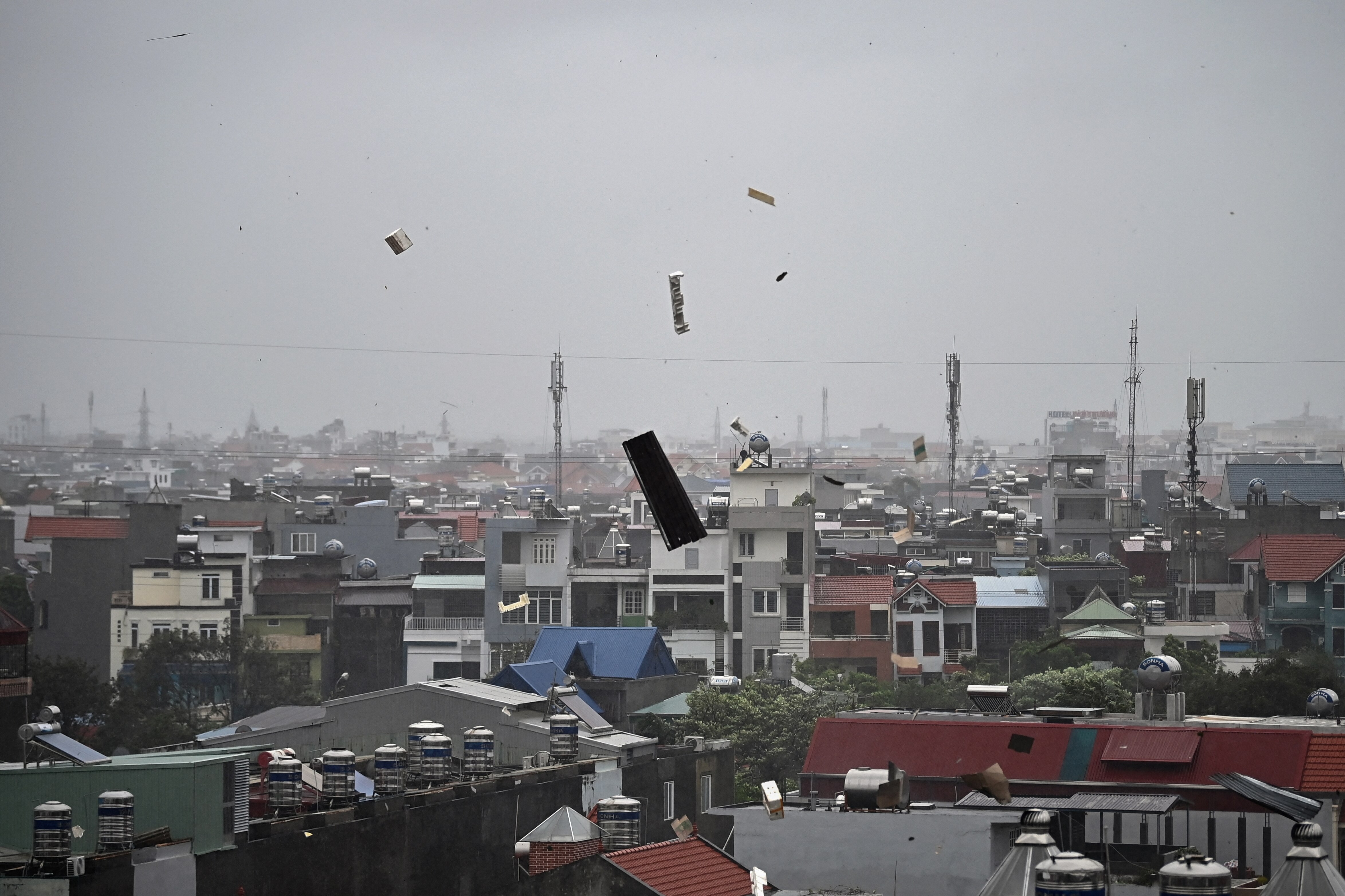 Bit of debris are seen flying in the air above a townscape, on grey sky.
