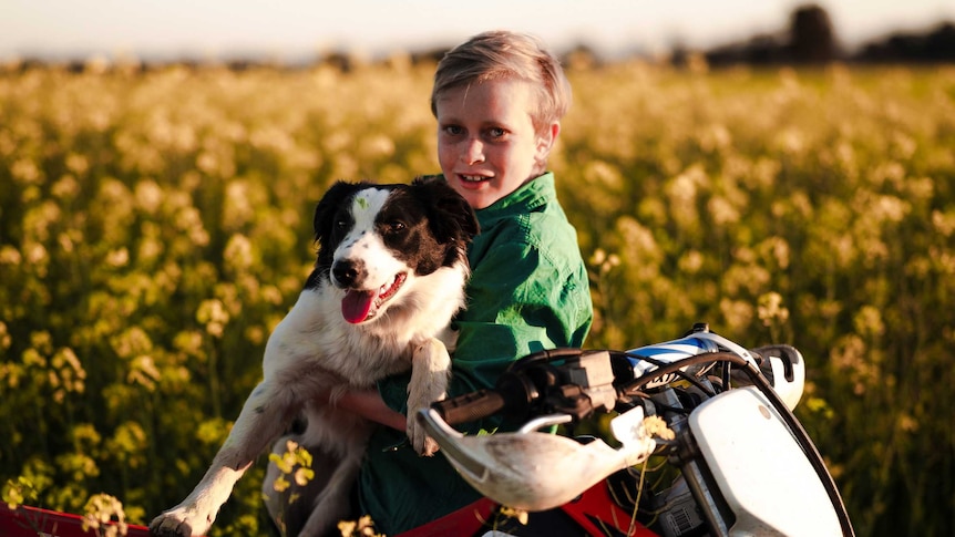 Teenager Hamish O'Brien sits on a motorbike holding his dog.