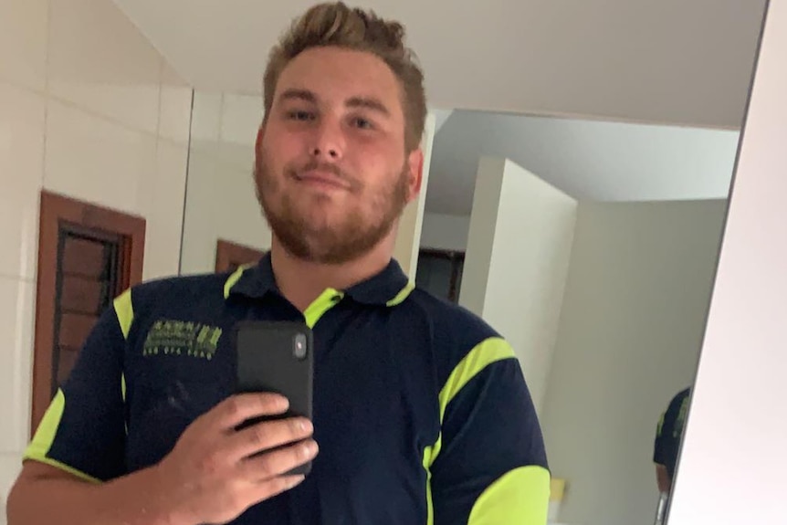 A man wearing a collared work shirt takes a selfie in a mirror