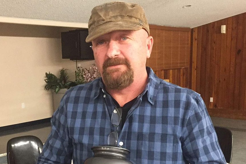 Stevan Utah in Canada, standing in a small auditorium holding an urn of ashes