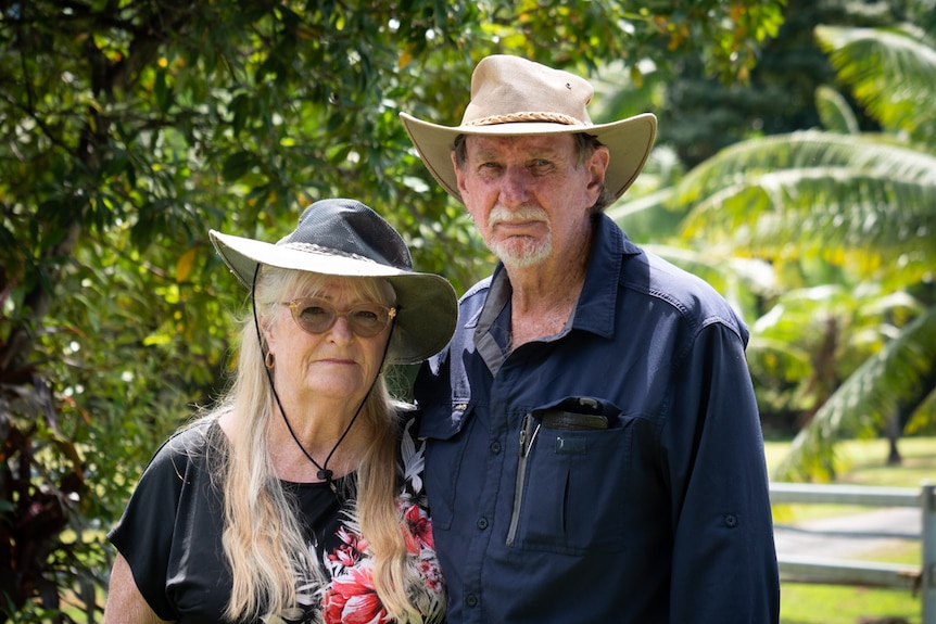 Sandra and Garry van Rees stand outside in front of a fence and lawn, with their arms around each other.