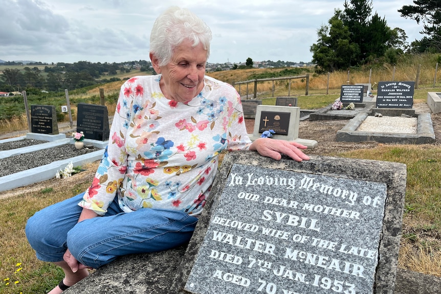 An elderly woman looks at gravestone 
