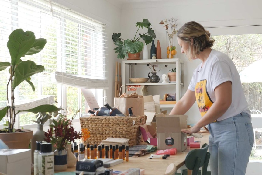 A blonde young woman packing boxes in her living room.