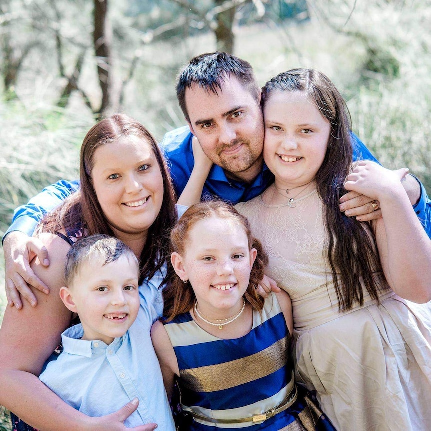 Jesse and her family smile in nice clothes for a family portrait. She has red hair and a big smile.