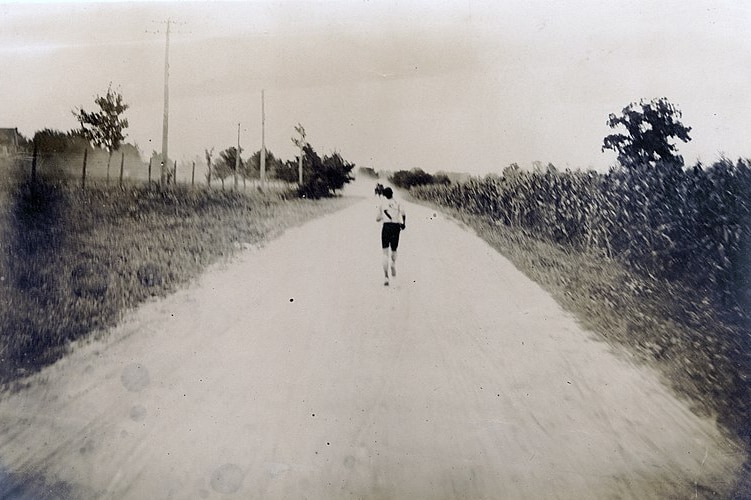 A black and white photo of a man running down a dusty country road