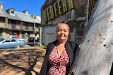 A woman leans against a tree with a Redfern sign behind her.