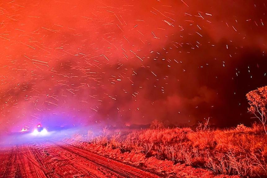 a bushfire at night, with the whole scene lit up red, sparks flying.