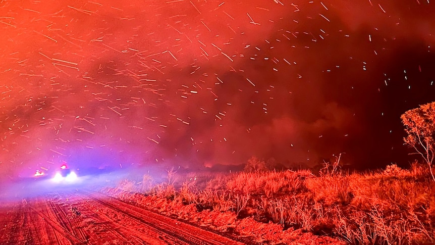 a bushfire at night, with the whole scene lit up red, sparks flying.