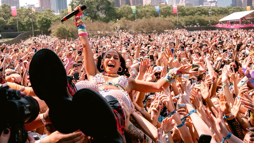 A woman holding a microphone looks at the camera while crowdsurfing on her back at a music festival