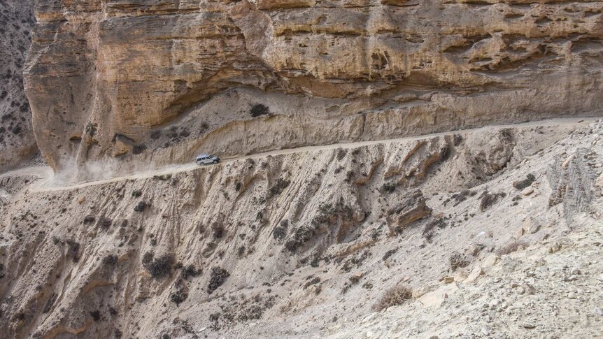 A jeep struggles precariously up a hill in a cliff face
