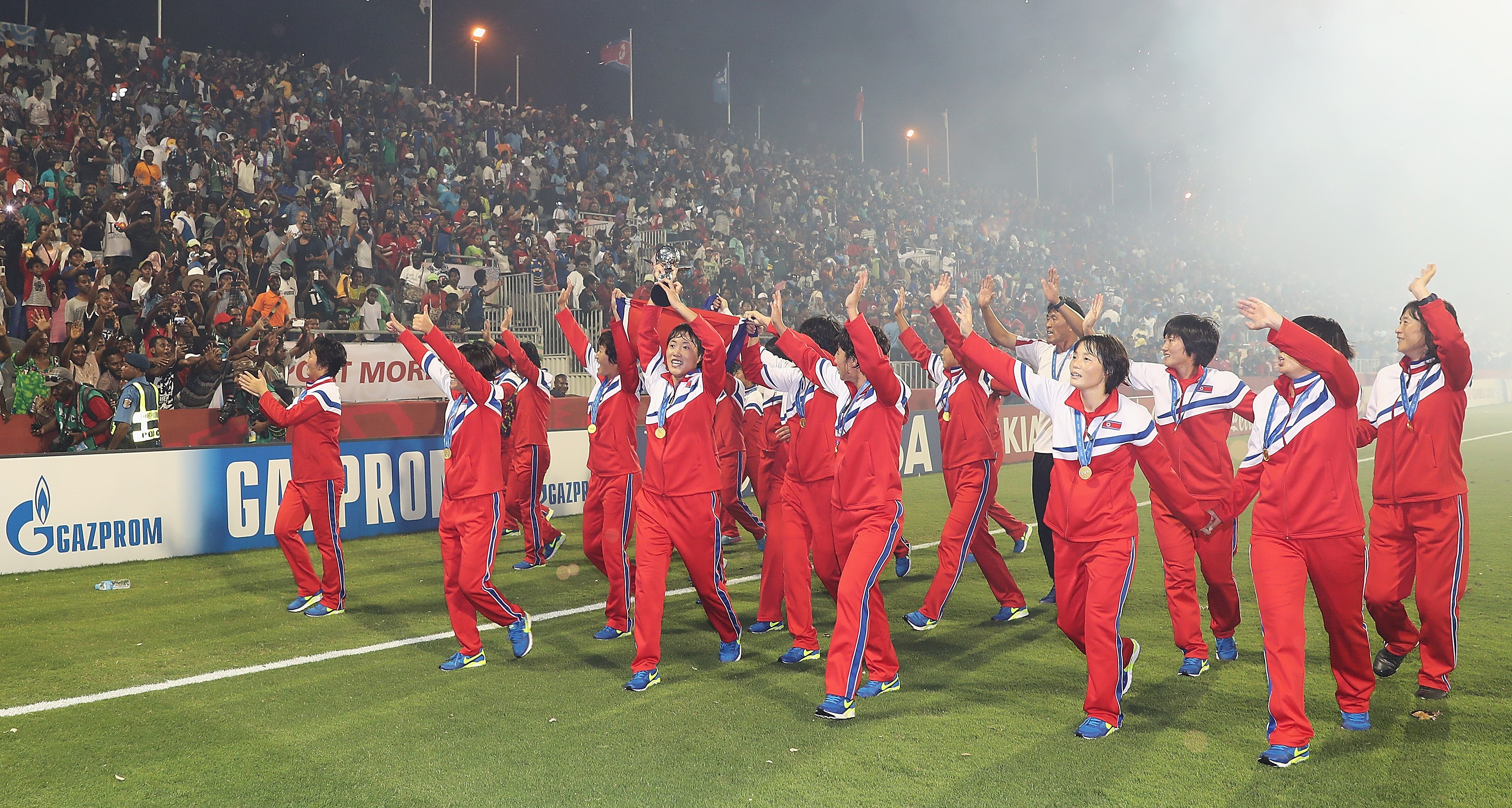 A soccer team wearing red, white and blue wave at a crowd after winning a soccer tournament