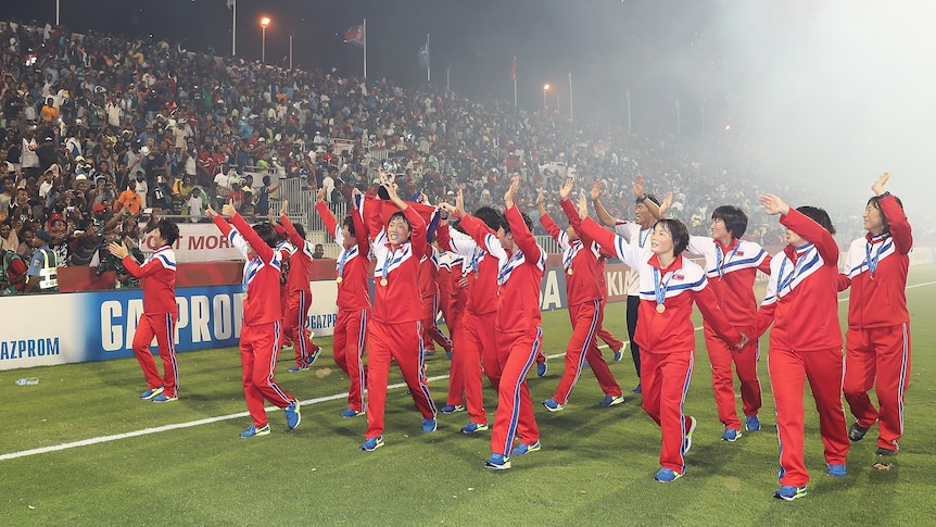 A soccer team wearing red, white and blue wave at a crowd after winning a soccer tournament