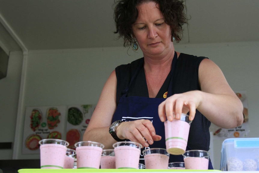 A woman holds one of several berry smoothie's she's made as she stands inside a food truck