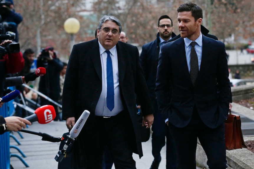 Former Real Madrid player Xabi Alonso arrives at a Madrid court flanked with reporters in a blue suit with an associate.