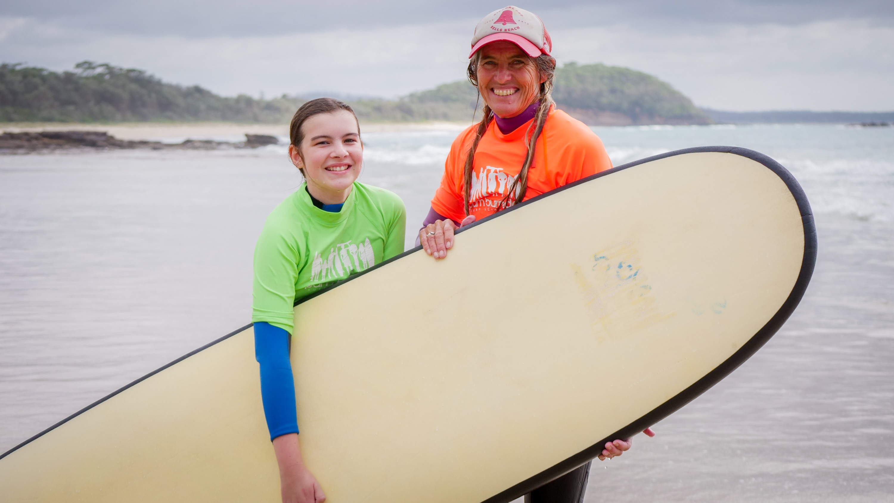 Young girl and older woman smiling on the beach holding surfboards