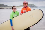 Young girl and older woman smiling on the beach holding surfboards