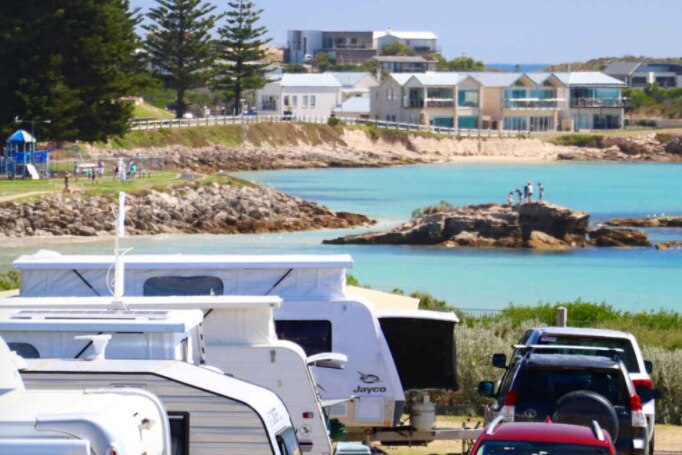Cars and caravans at the forefront with the ocean and houses behind