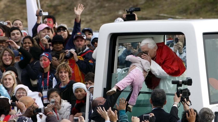 The Pope kisses a baby through the open window of his Popemobile.